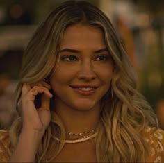 a woman talking on a cell phone while wearing a yellow dress and gold necklaces