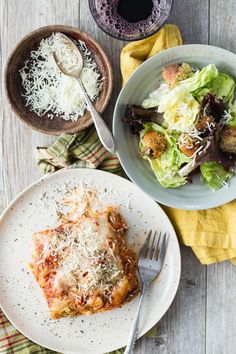 a white plate topped with lasagna next to a bowl of salad and fork