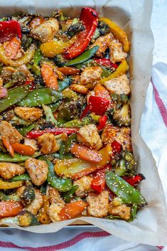 a pan filled with chicken, peppers and broccoli covered in sesame seed flakes