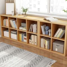 a bookshelf filled with lots of books in front of a window next to a rug