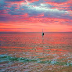 a lighthouse in the middle of an ocean with pink and blue clouds above it at sunset