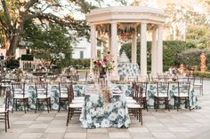 an outdoor wedding reception with floral tablecloths and chairs set up in front of a gazebo