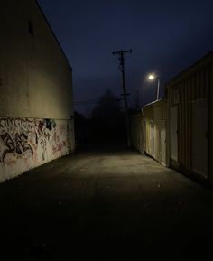 a dark alley way with graffiti on the wall and street lights in the background at night