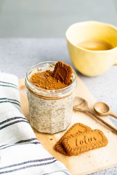 a jar of peanut butter next to a cookie on a cutting board with spoons