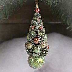 a christmas tree ornament hanging from a pine tree with snow on the ground