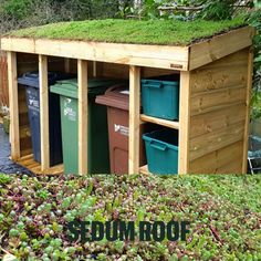 an outdoor storage shed with grass growing on top and trash cans in the bins