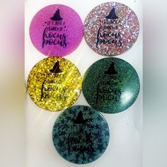 four different colored buttons with witches sayings and glitter on them, all in the same color