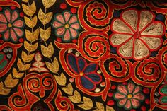 an intricately decorated cloth with flowers and leaves on it's side, in red