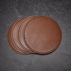 three brown leather coasters sitting on top of a black table next to each other