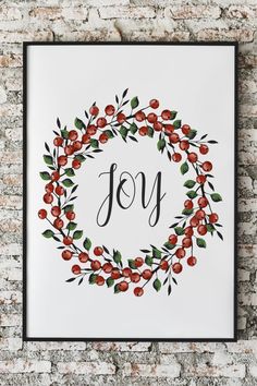 a framed print with the word joy surrounded by red berries and leaves on a white brick wall