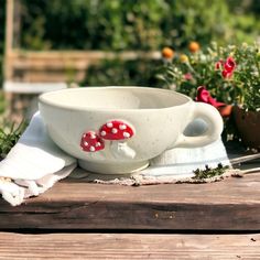 a white bowl with red mushrooms on it sitting on top of a wooden table next to potted plants