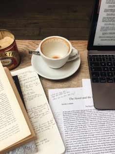 an open book next to a cup of coffee and a laptop on a wooden table