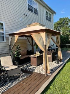 a gazebo sitting on top of a wooden deck in front of a house next to a lawn