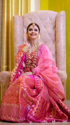 a woman sitting on top of a chair wearing a pink sari and gold jewelry