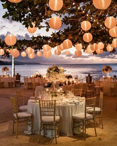 an outdoor dining area with paper lanterns hanging from the ceiling and tables covered in white linens