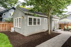 a small gray house with a tree in the yard