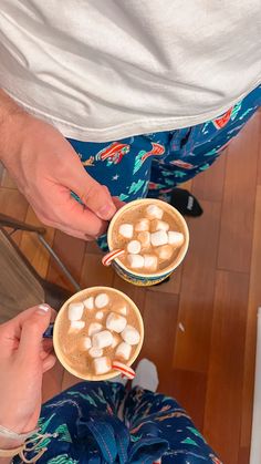 two people holding cups with marshmallows in them