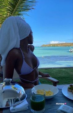 a woman wearing a towel on her head sitting at a table with food and drinks