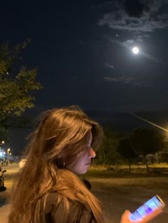 a woman is looking at her cell phone while the moon shines in the sky