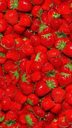 a large pile of red strawberries with green leaves on the top and bottom half