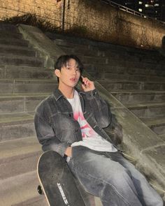 a young man sitting on steps talking on his cell phone while holding a skateboard