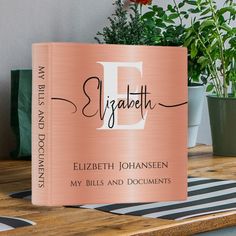 a pink book sitting on top of a wooden table next to a potted plant