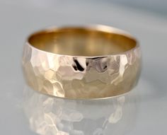 a close up of a gold wedding ring on a white surface with reflective reflection in the background