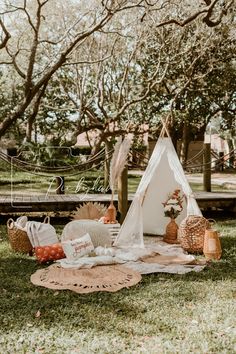 a teepee tent set up in the grass with pillows and blankets on it, surrounded by trees