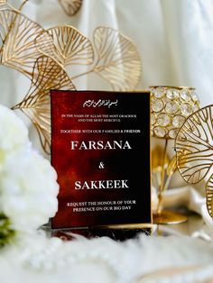 the wedding card is on display next to some white flowers and gold fan shaped decorations