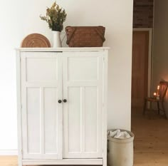 a white cabinet sitting next to a wall with a basket on top of it and candles in the background