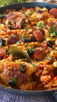 a pan filled with rice, meat and olives on top of a wooden table