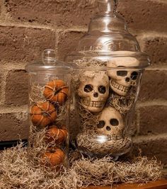 two glass jars filled with skulls sitting on top of dry grass next to pumpkins