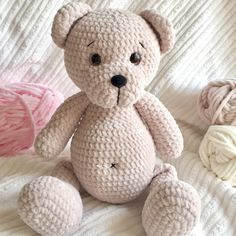 a crocheted teddy bear sitting on top of a bed next to balls of yarn