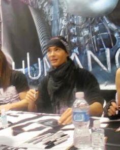 three people are sitting at a table with water bottles and pens in front of them