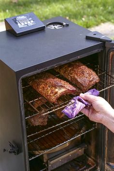 someone is pulling out some meat from an outdoor grill with the door open and it's being grilled