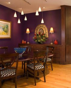 a dining room with purple walls and wooden flooring is lit by pendant lights that hang from the ceiling