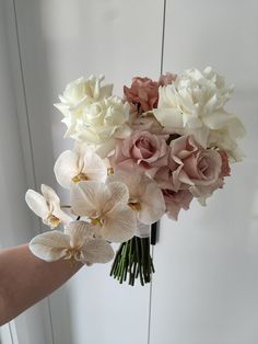 a hand holding a bouquet of flowers in front of a white wall with mirrors behind it