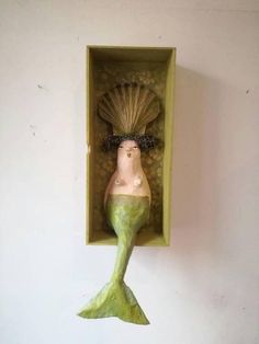 a ceramic sculpture of a mermaid in a box on the wall, with its tail sticking out