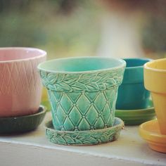 several different colored cups and saucers on a window sill with trees in the background