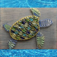 a sea turtle made out of wire sitting on top of a wooden board next to a swimming pool