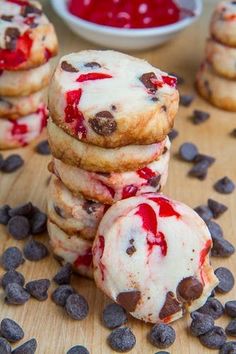 cookies with chocolate chips and raspberry filling on a cutting board next to bowls of cherries