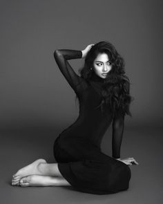 a woman is sitting on the floor posing for a black and white photo with her hands behind her head