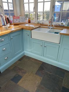 a kitchen with blue cabinets and wooden counter tops is shown in this image, there are books on the window sill