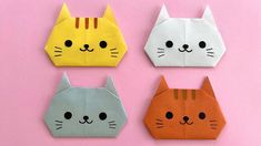 four origami cats sitting next to each other on a pink surface with one cat's face cut out