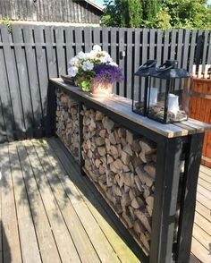 a firewood bar on a deck with flowers in the vase and an old lantern