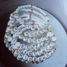 several white and gold beaded bracelets with words on them sitting on a plate