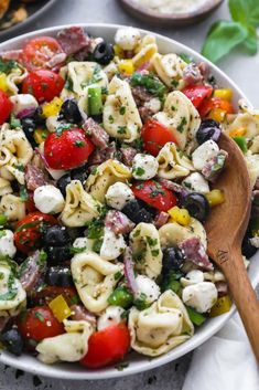 a bowl filled with pasta salad and a wooden spoon