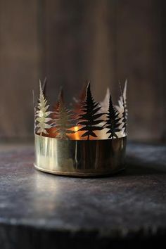 a gold crown with trees on it sitting on top of a wooden table next to a candle