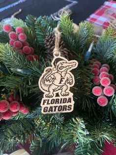 a florida gators ornament hanging from a christmas tree with pine cones and red berries