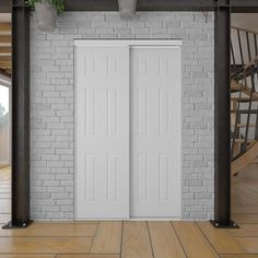 two white doors in front of a brick wall and wooden stairs with potted plants